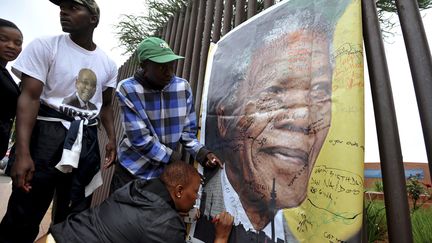 Les passants se pressent pour &eacute;crire des messages sur un poster de Nelson Mandela. L'affiche est accroch&eacute;e &agrave; des grilles de la rue&nbsp;Vilakazi, &agrave; Soweto en Afrique du Sud, o&ugrave; Nelson Mandela a v&eacute;cu de nombreuses ann&eacute;es. (REUTERS)