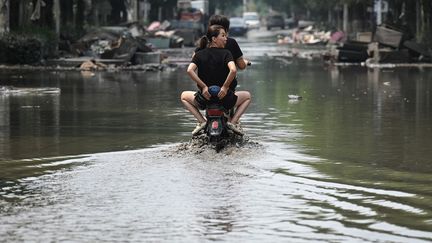 Deux personnes sur un scooter dans une rue inondée de Zhuozhou (Chine), le 9 août 2023. (JADE GAO / AFP)