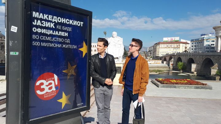 Deux jeunes étudiants, partisans du "OUI" devant une affiche incitant à voter. L'affiche dit : "Votez OUI. La langue macédonienne va devenir officielle dans la famille de 500 millions d'habitants". (MARIE-PIERRE VEROT / RADIO FRANCE)