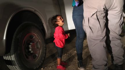 Une Hondurienne de deux ans pleure pendant que des forces de police fouillent sa mère, le 12 juin 2018 à McAllen, à la frontière entre les Etats-Unis et le Mexique.&nbsp;Une "caravane" de migrants honduriens s'était dirigée à pied vers les Etats-Unis à l'automne de cette même année. En réaction, Donald Trump avait annoncé le déploiement de l'armée américaine à la frontière. (JOHN MOORE / GETTY IMAGES NORTH AMERICA / AFP)