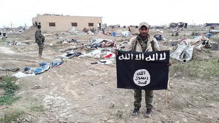 Un combattant des FDS&nbsp;brandit le drapeau de Daech qui flottait sur une position reprise aux jihadistes à Baghouz (Syrie), le 15 mars 2019. (AURÉLIEN COLLY / RADIO FRANCE)