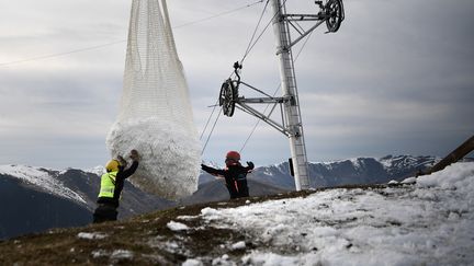 Deux hommes réceptionnent la neige apportée par un hélicoptère pour réenneiger un téléski dans la station pyrénéenne de Luchon-Superbagnères, le 15 février 2020. (ANNE-CHRISTINE POUJOULAT / AFP)