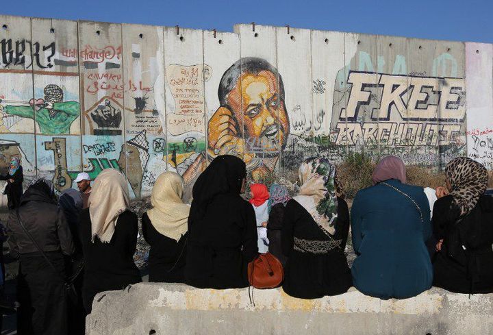 Des femmes palestiniennes, assises près du mur de séparation entre Ramallah et Jérusalem, sur lequel figure un dessin appelant à la libération du prisonnier Marwan Barghouti.  (Abbas Momani-AFP)