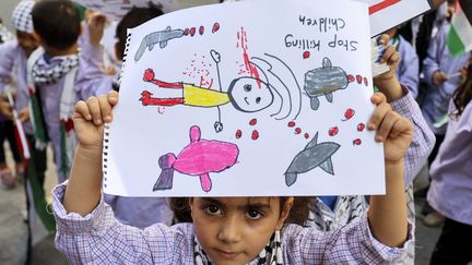 Un enfant palestinien réfugié au Liban montre son dessin lors d'un sit-in devant la Croix-Rouge internationale à Beyrouth. Il y est écrit : "Arrêtez de tuer des enfants !". Photo d'illustration. (ANWAR AMRO / AFP)