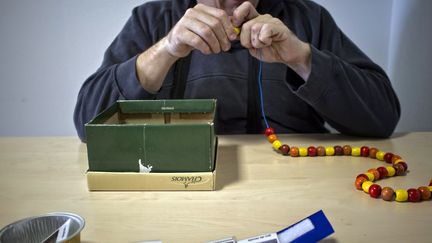 Une personne autiste r&eacute;alise un collier de perles avec l'aide du personnel du centre m&eacute;dical "l'Envol&eacute;e", &agrave; l'Isle d'Abeau dans l'Is&egrave;re,&nbsp;le 5 mars 2012. (JEAN-PHILIPPE KSIAZEK / AFP)