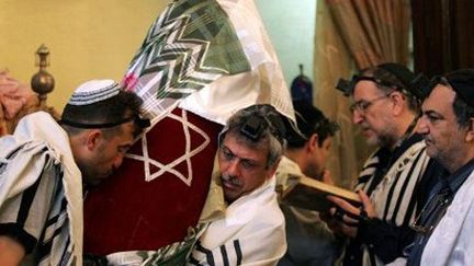 Dans une synagogue du Téhéran, un fidèle, couvert d'une kippa et d'un châle de prière, porte la Torah. Un autre lit un texte sacré.  (AFP - Hassan Ammar)