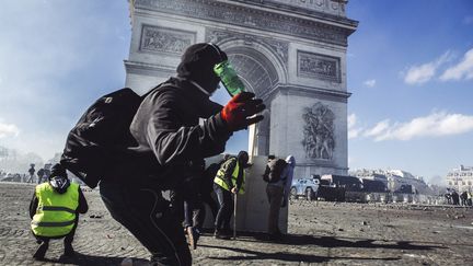 Un manifestant&nbsp;cagoulé s'apprête à lancer une bouteille sur les forces de l'ordre, devant l'Arc de triomphe à Paris, le 16 mars 2019.&nbsp; (YANN CASTANIER / HANS LUCAS / AFP)