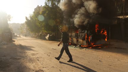 Un syrien marche &nbsp;devant un bus en feu à Alep en Syrie, le 25 septembre 2016. (AMEER ALHALBI / AFP)