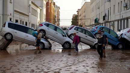 Des habitants marchent devant des voitures empilées après les inondations meurtrrières à Sedaví, une commune de la province de Valence, en Espagne, le 30 octobre 2024. (MANAURE QUINTERO / AFP)