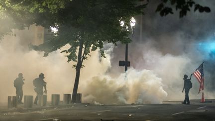 Des agents fédéraux (à gauche) font face à un manifestant qui porte un drapeau des Etats-Unis, le 21 juillet 2020 à Portland (Oregon). (NATHAN HOWARD / GETTY IMAGES NORTH AMERICA / AFP)