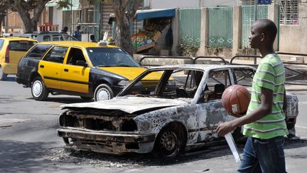 A Dakar, un jeune S&eacute;n&eacute;galais passe devant une voiture incendi&eacute;e pendant les violences survenues dans la nuit du 27 au 28 janvier 2012. (SEYLLOU /&nbsp;AFP PHOTO)