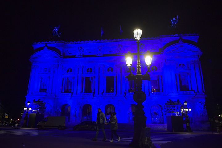 Un couple marche à quelques pas de l'Opéra Garnier éclairé en bleu, couleur du drapeau de l'UE, le 2 janvier 2022 à Paris (JULIEN DE ROSA / AFP)