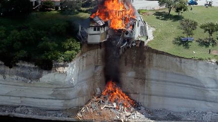 Une maison, qui mena&ccedil;ait de s'effondrer apr&egrave;s un glissement de terrain sur les bords du lac Whitney (Texas, Etats-Unis), br&ucirc;le apr&egrave;s avoir &eacute;t&eacute; incendi&eacute;e volontairement le 13 juin 2014. (BRANDON WADE / REUTERS)