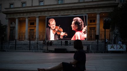 Une femme regarde un concert dirigé par&nbsp;Thomas Hengelbrock, sur la place de Verdun, à Aix-en-Provence. Une partie de l'édition 2020 du festival a été annulée à cause de la pandémie.&nbsp; (CLEMENT MAHOUDEAU / AFP)