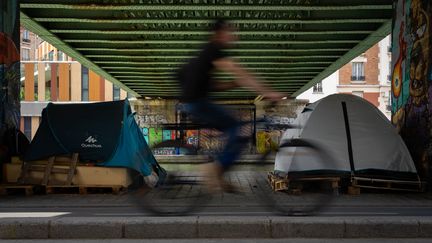 Un cyliste passe devant deux tentes de sans-abris sous la passerelle du bassin de la Villette à Paris le 3 juin 2020. (ANTOINE DE RAIGNIAC / HANS LUCAS / AFP)