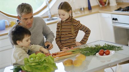 Une fille et un garçon cuisinent avec leur père. (MAXPPP)