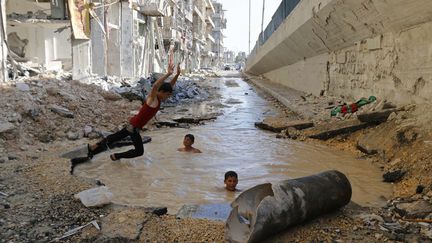 De jeunes gar&ccedil;ons s'amusent dans un crat&egrave;re rempli d'eau &agrave; Alep (Syrie), le 10 juillet 2014. (HOSAM KATAN / REUTERS)