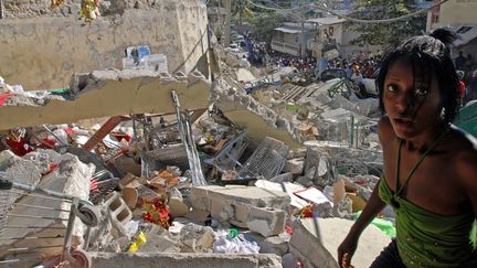 Une jeune femme ère, hagarde, au milieu de ruines d'un immeuble de Port-au-Prince, le 13 janvier 2010. La veille, un séisme d'une magnitude de 7,3 sur l'échelle de Richter a ravagé la capitale du pays, faisant plus&nbsp;de 300 000 morts et autant de blessés. (THONY BELIZAIRE / AFP)