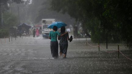 Des femmes marchent sous la pluie, dans le bidonville de&nbsp;Shwegyin, dans la région de Bago, le 8 août 2019. (YE AUNG THU / AFP)