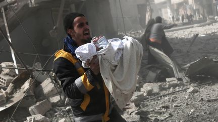 Un Syrien sauve un enfant des ruines d'un immeuble, dans la région de la Ghouta en Syrie, le 13 février 2018. (AFP)