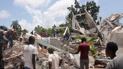 Des habitants devant des décombres dans la ville des Cayes, après le puissant séisme qui a frappé Haïti, le 14 août 2021. (STANLEY LOUIS / AFP)