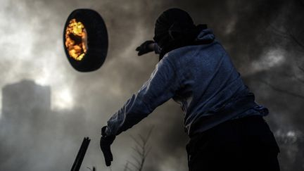 Un manifestant en train de monter une barricade jette un pneu enflammé en direction de la police, à Kiev (Ukraine), le 21 février 2014.
 (Bulent Kilic / AFP)