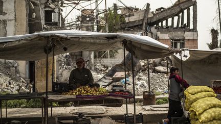 Un vendeur de fruits et légumes attend ses clients dans un magasin improvisé devant des bâtiments détruits dans la ville syrienne du nord de Raqa, ancienne capitale syrienne du groupe État islamique (EI), le 14 avril 2019. (DELIL SOULEIMAN / AFP)