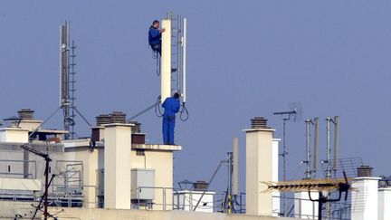 Des techniciens installent des relais téléphoniques sur le toit d'un immeuble, à Paris. (JACQUES DEMARTHON / AFP)