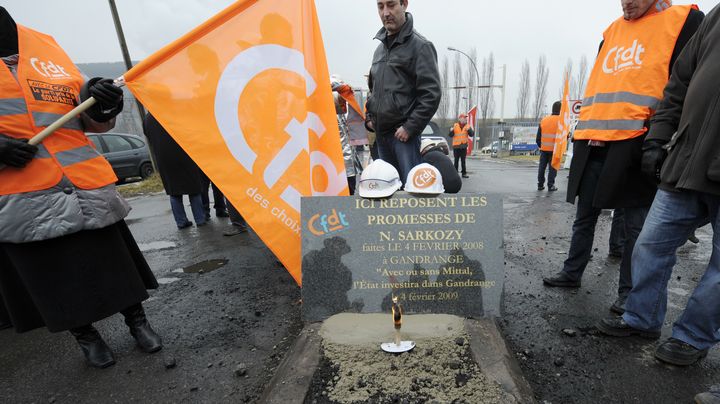 Les salari&eacute;s de Gandrange&nbsp;(Moselle) posent devant la plaque comm&eacute;morative des promesses non-tenues de Nicolas Sarkozy. (JEAN-CHRISTOPHE VERHAEGEN / AFP)