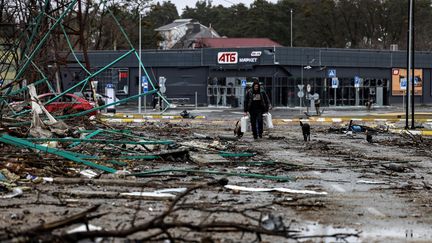 Un homme marche dans une rue dévastée de Boutcha (Ukraine) avec des sacs de vivres donnés par l'armée ukrainienne, après le départ des soldats russes, le 2 avril 2022. (RONALDO SCHEMIDT / AFP)