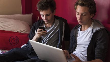 Deux adolescents consultent leur ordinateur et smartphone, à Paris, le 5 août 2015. (NATHAN ALLIARD / PHOTONONSTOP AFP)