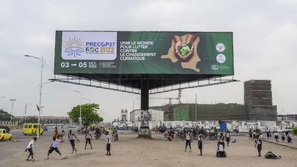 Des enfants jouant à Kinshasa, en République démocratique du Congo (RDC), le 23 septembre 2022 devant une affiche annonçant&nbsp;la réunion préparatoire de la COP27 (pré-COP27). La conférence sur le climat se tiendra&nbsp;en novembre 2022 en Egypte.&nbsp; (ARSENE MPIANA / AFP)