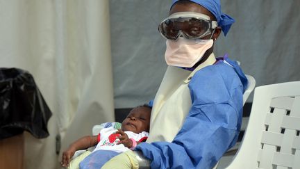 Un membre du personnel m&eacute;dical tient dans ses bras un b&eacute;b&eacute; victime d'Ebola. L'enfant est soign&eacute; dans un centre de M&eacute;decins sans fronti&egrave;res &agrave; Monrovia (Liberia), le 18 octobre 2014. (ZOOM DOSSO / AFP)