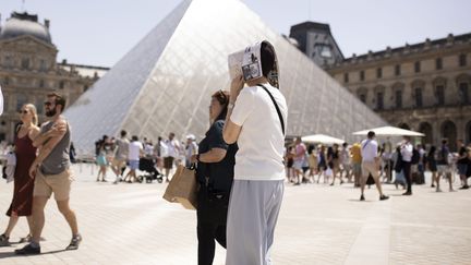 Une femme se protège du soleil à l'aide d'un plan de Paris devant la pyramide du musée du Louvre, le 17 juin 2022. (ALEXIS SCIARD / MAXPPP)