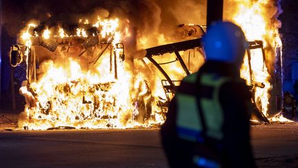 Un policier anti-émeutes se tient près d'un bus en flammes&nbsp;à Malmö (Suède), le 16 avril 2022. (JOHAN NILSSON / TT NEWS AGENCY / AFP)