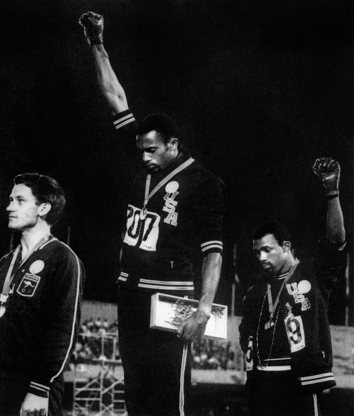 Les athlètes américains Tommie Smith (au centre) et John Carlos (à droite) lèvent un poing ganté en soutien aux mouvements des droits civiques aux Etats-Unis, lors des Jeux olympiques de Mexico, le 17 octobre 1968. (AFP / EPU)