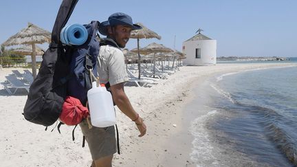 Ce jeune ingénieur en génie sanitaire s'est mis en route début juillet avec son sac à dos et sa guitare pour un périple de deux mois visant à sensibiliser autorités et vacanciers à l'importance de ne pas faire de la mer une poubelle. Chapeau couvrant son maigre visage buriné et brodequins aux pieds, le jeune homme de 27 ans est parti de Mahdia (est). Il terminera son parcours sur la plage de Soliman, à 40 km de Tunis, la capitale, après avoir nettoyé des plages bondées comme celle de Dar Chaabane à Nabeul mais aussi de petites criques plus secrètes.
 (FETHI BELAID / AFP)