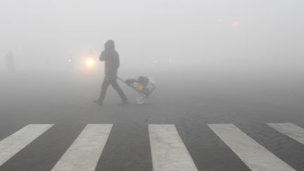 Un piéton traverse une rue couverte par un nuage de particules-fines, à Lianyungang,&nbsp;dans l'est de la Chine, le 19 décembre 2016. (STR / AFP)