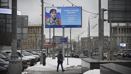 Un homme marche à côté d'un panneau d'affichage présentant un soldat russe participant à la guerre en Ukraine, à Moscou le 15 février 2023. (ALEXANDER NEMENOV / AFP)