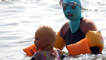 Non il ne s'agit pas d'un hommage au Pussy Riot mais d'une baigneuse chinoise et son enfant portant un "face-kini" sur une plage de Qingdao (Chine), le 16 ao&ucirc;t 2012. Une mani&egrave;re de se prot&eacute;ger du soleil, des m&eacute;duses, des insectes etc. Et du ridicule ? (AFP)