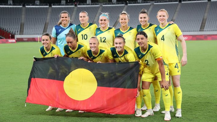 L'équipe australienne et la gardienne Lydia Williams (en haut à droite) brandissant le drapeau indigène lors des Jeux olympiques à Tokyo, le 21 juillet 2021. (YOSHIKAZU TSUNO / AFP)