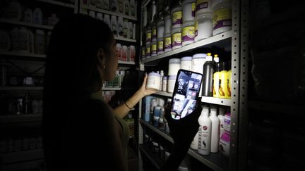 Une employée d'un magasin de cosmétiques s'éclaire avec son téléphone, à Caracas (Venezuela), lors d'une vaste coupure de courant, le 30 août 2024. (PEDRO RANCES MATTEY / AFP)