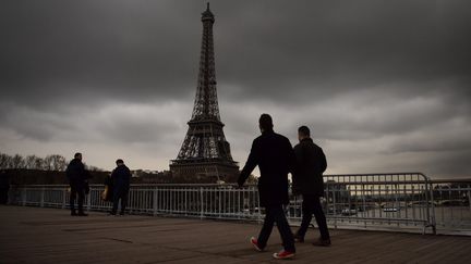 Des badauds marchent sur un pont près de la tour Eiffel, à Paris, le 6 janvier 2018, sous un ciel menaçant.&nbsp; (CHRISTOPHE SIMON / AFP)