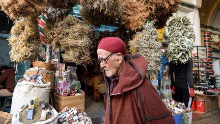 Vieil homme marchant à côté d'un commerce de plantes médicinales dans le souk el-Blat, dans la vieille ville de Tunis, le 14 mars 2020. (FETHI BELAID / AFP)