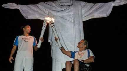 Sur cette photo, le judoka brésilien Rafaela Silva, qui a gagné une médaille d'or aux JO de Rio, reçoit la flamme olympique de l'écrivain brésilien, Thomas Magalhaes, devant la statue du Christ Rédempteur, à Rio, le 6 septembre 2016. (YASUYOSHI CHIBA / AFP)