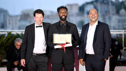 Ladj Ly (au centre) accompagné des producteurs Christophe Barral (à gauche) et Toufik Ayadi (à droite), lors de la remise des prix de la 72e édition du festival de Cannes, le 25 mai 2019. (LOIC VENANCE / AFP)