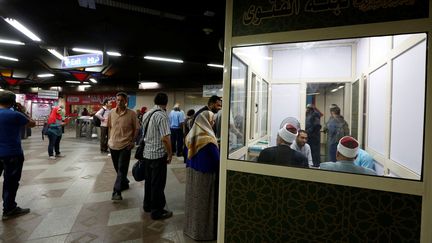 Matériellement, selon le correspondant de RFI en Egypte, c'est une sorte de local en verre borduré d'aluminium de trois mètres sur deux, installé à proximité des portillons du métro. A l'intérieur, deux cheikhs détachés par le centre de recherches islamiques de la mosquée d'Al-Azhar, plus haute autorité de l'Islam sunnite. Un troisième siège est réservé aux voyageurs souhaitant obtenir une consultation en matière de jurisprudence islamique avant de prendre le métro. Un métro qui accueille chaque jour 5 millions de voyageurs. Les internautes ont aussitôt tourné ces cheikhs en dérision, les comparant à des vendeurs ambulants. Jugeant l'initiative aussi inutile que risible, ils suggèrent ironiquement de prolonger le kiosque par un confessional pour les chrétiens qui constituent 10% de la population. Cautionnées par les autorités politiques, les autorités religieuses, vexées, ont accusé les internautes de mauvaise foi et rappellent que ces kiosques sont destinés à combattre l'extrémisme religieux..
	  (REUTERS/Amr Abdallah Dalsh)