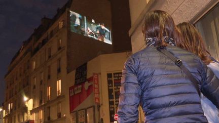 Spectateurs dans la rue Daubanton qui regarde un film sur la façade du cinéma La Clef (France 3 Paris Ile de France)