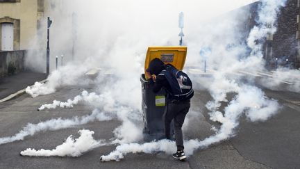 Un manifestant se protège derrière une poubelle à Rennes (Ille-et-Vilaine), le 17 mai 2016 pendant la manifestation contre la loi Travail, alors que des grenades lacrymogènes tombent à ses pieds. (DAMIEN MEYER / AFP)