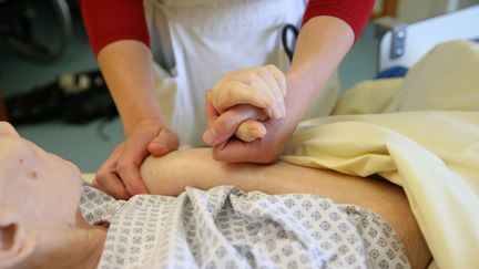 Les mains d'un docteur tiennent celles d'une personne en fin de vie, à Colmar. (VANESSA MEYER / MAXPPP)